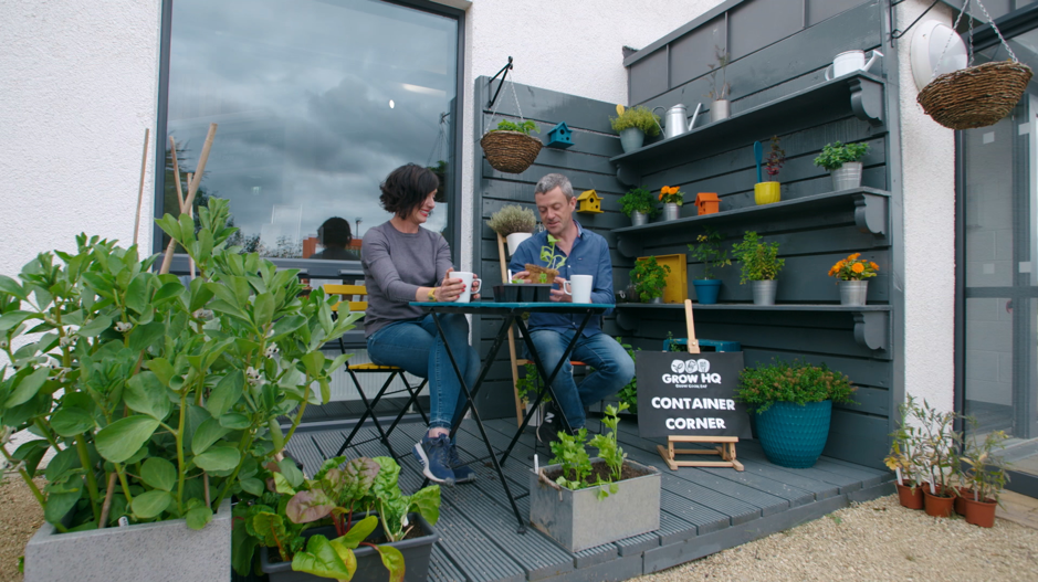 A woman and a man sitting at a table outside surrounded by containers of vegetables